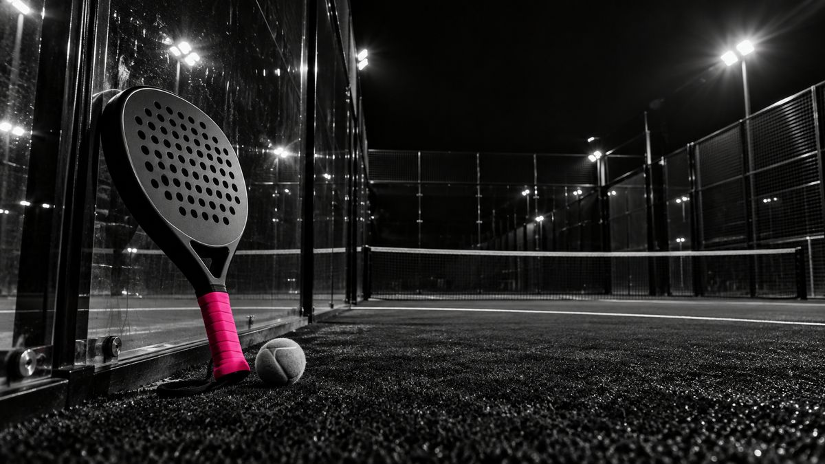 Cancha de pádel de vidrio de noche: pala con grip magenta apoyada en el cristal